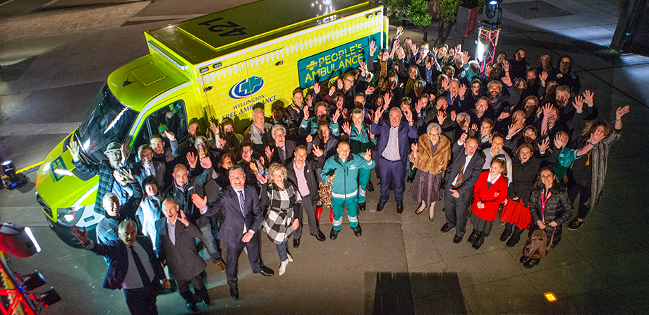Members of the public alongside staff from Wellington free ambulance, outside an ambulance and waving at camera