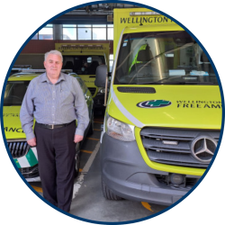 A man in a grey shirt stands in front of an ambulance