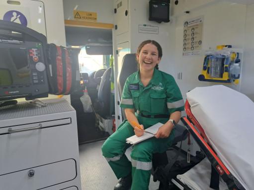 A young woman in a green paramedic uniform sits inside an ambulance