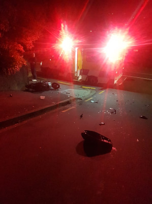 An ambulance with red lights on a dark street with pieces of moped on the pavement in front of it