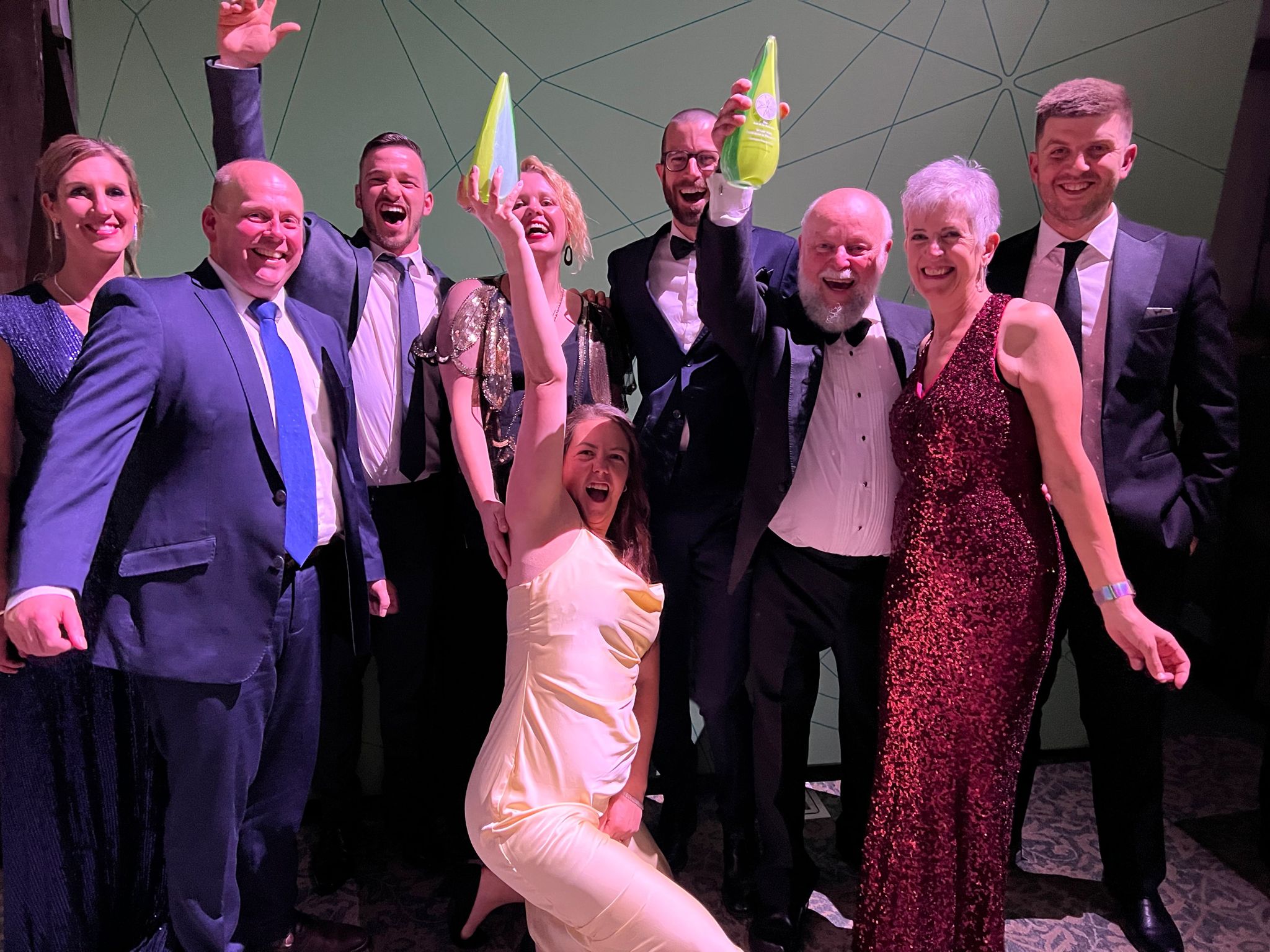 A group of people in black tie hold up 3 awards