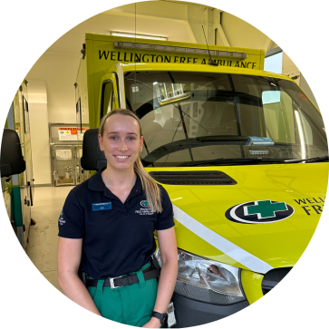 A woman with a blonde ponytail in front of an ambulance