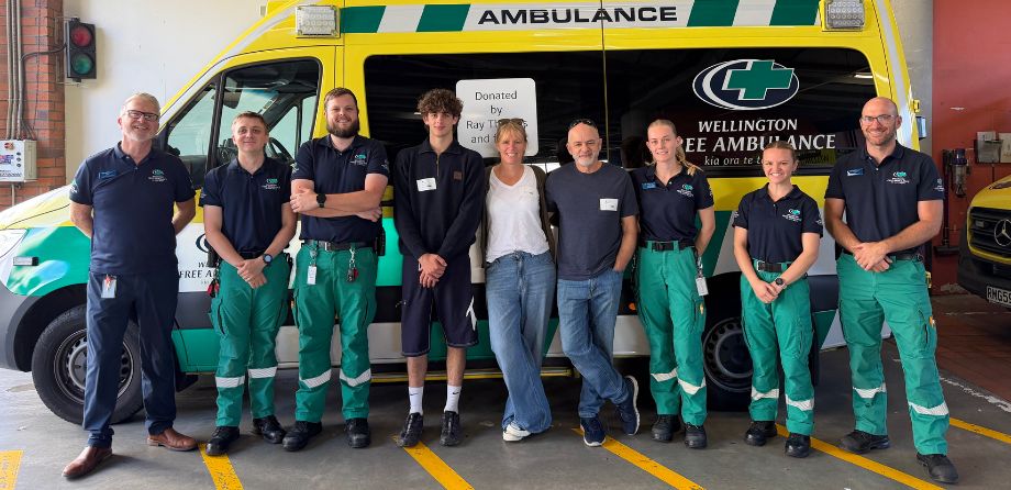 A group of paramedics and people smile in front of an ambulance