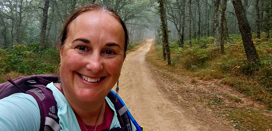 A woman with a purple backpack smiles in a forest