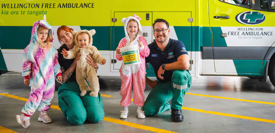 2 paramedics and children in onesies smile in front of an ambulance