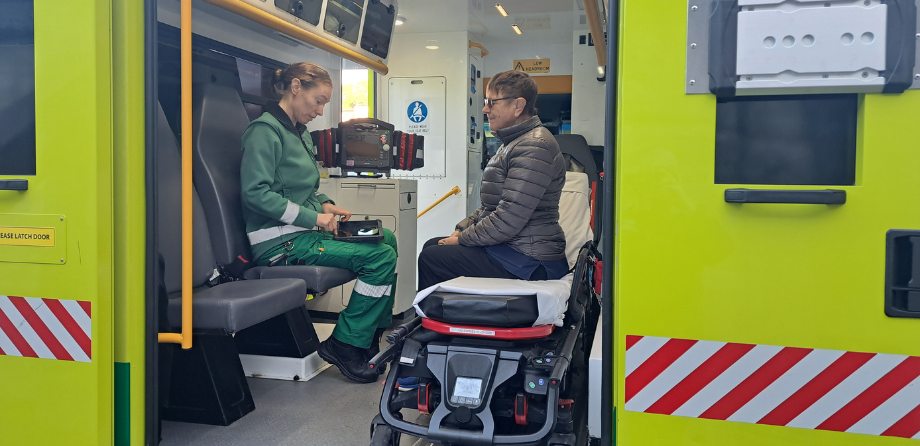 A paramedic makes notes on a tablet while sat opposite a patient in the back of an ambulance