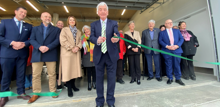 A man in a dark blue suit cuts a green ribbon
