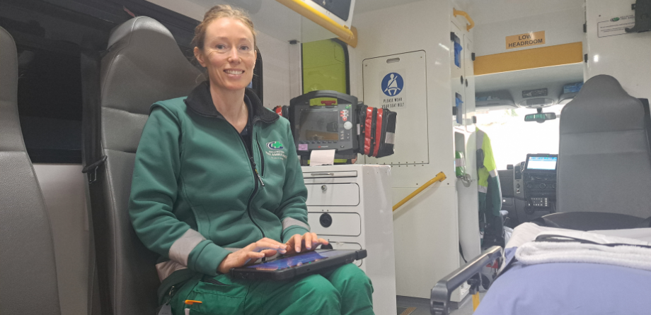 A paramedic sitting in the back of an ambulance smiles