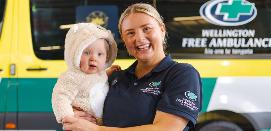 A paramedic holds a baby in a onesie