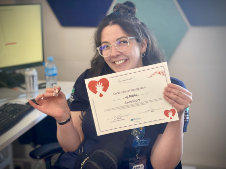 A person with long dark hair and glasses smiles with a certificate