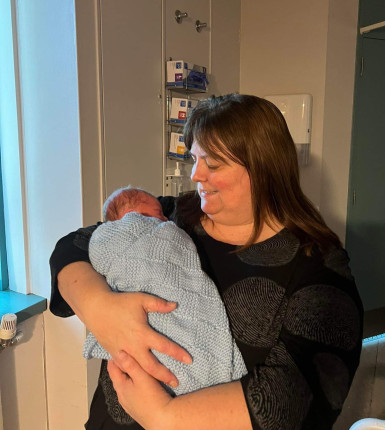 A woman with brown hair holds a baby wrapped in a blue blanket