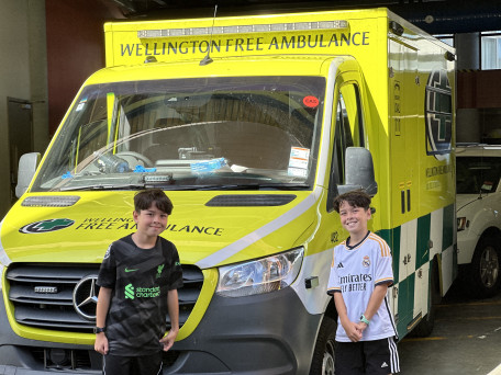 2 young boys in football kit stand in front of an ambulance