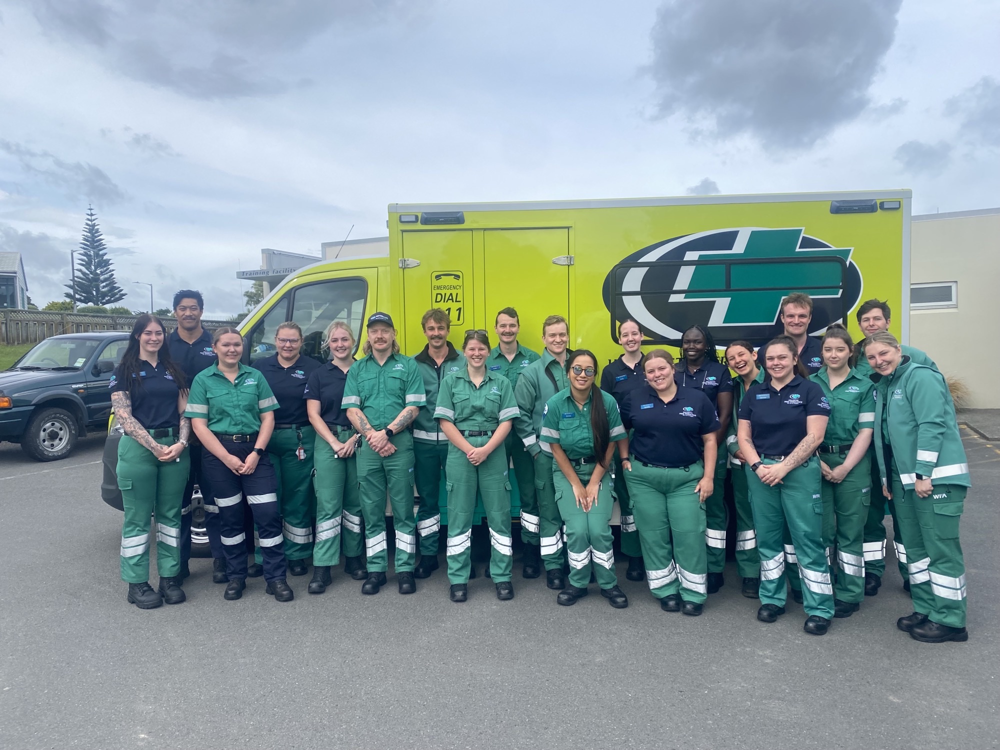 A group of men and women in green Wellington Free Ambulance uniform stand in front of an ambulance
