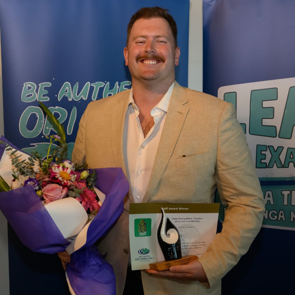 A man holds a bouquet, certificate and trophy