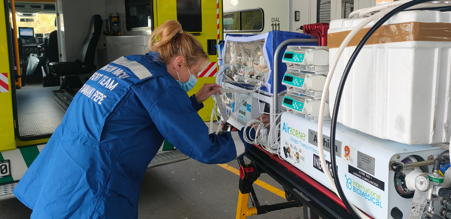 A nurse tends to a baby in an incubator, on a stretcher