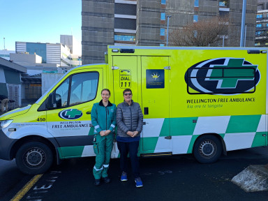 A paramedic and a patient smile in front of an ambulance