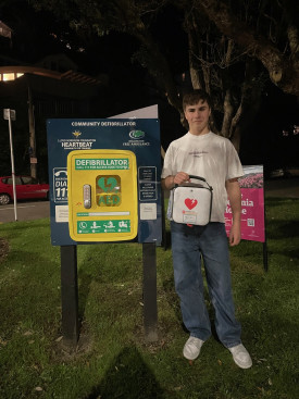 A teenage boy holds an AED next to a cabinet