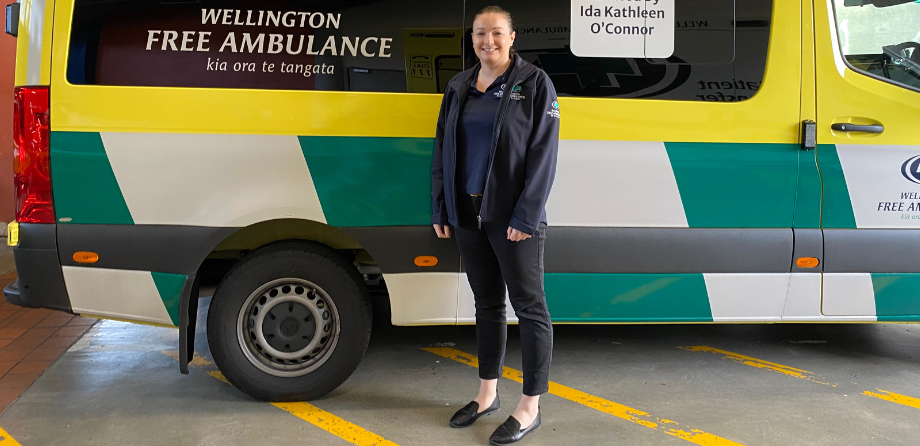 A woman in a dark blue jacket smiles in front of an ambulance