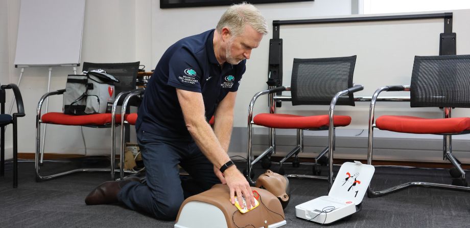 A man in a dark blue polo applies AED pads to a mannikin
