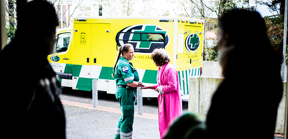 Two people in shadow at the front of the photo in the background a woman has her hand on a paramedics arm